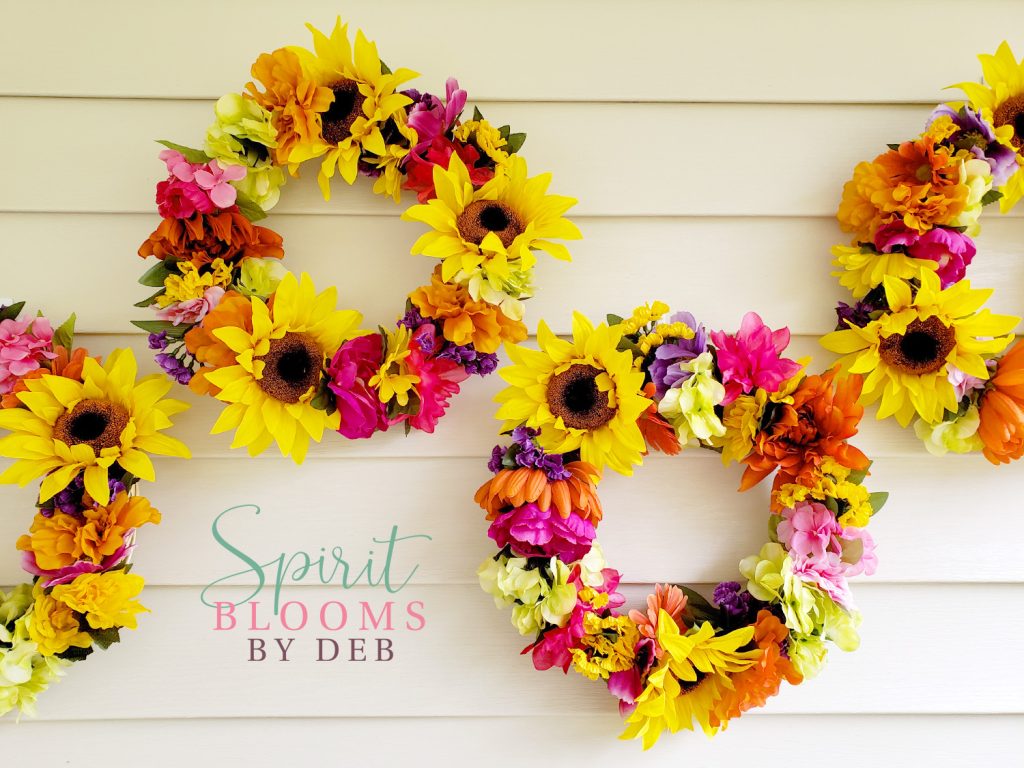 Arrangement of four colorful wreaths with sunflowers on an outdoor wall.