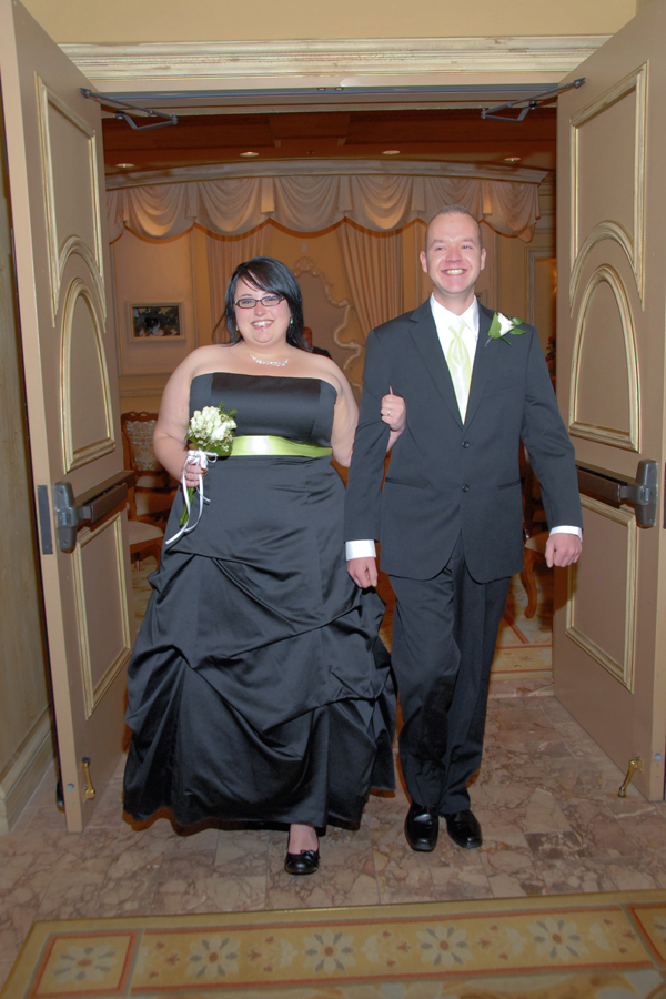 Woman and man wearing black wedding clothes and smiles leaving the Luxor Chapel after wedding ceremony, Las Vegas.