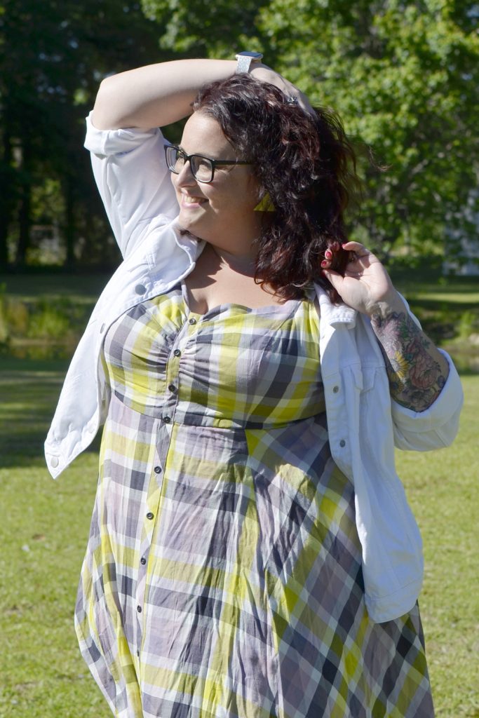 Maranda, a plus size woman, smiles into the sun wearing a plaid Torrid dress with white denim jacket for Outfit of the Day.