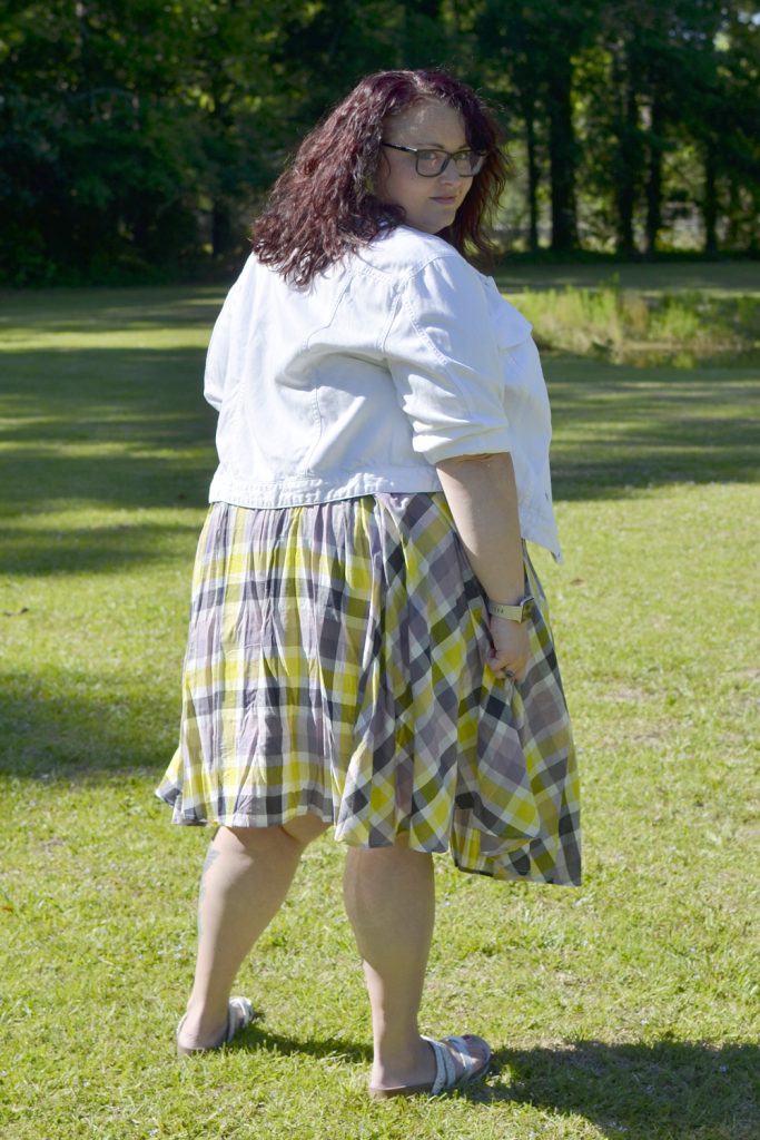 Maranda, a plus size woman, facing away from the camera wearing a plaid Torrid dress with white denim jacket.