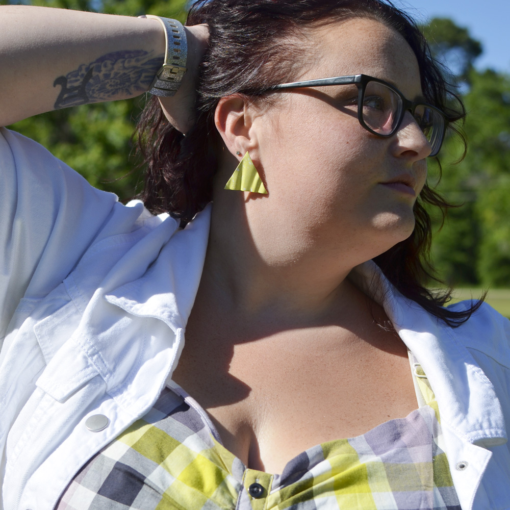 Maranda, a plus size woman with glasses, holds hair back to model yellow triangle statement earrings.