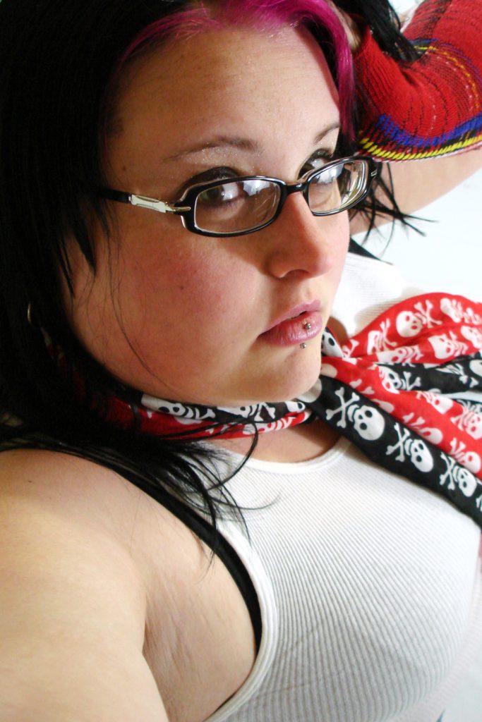 Side profile shot of chubby punk girl with black and pink hair wearing skull scarves and punk accessories.