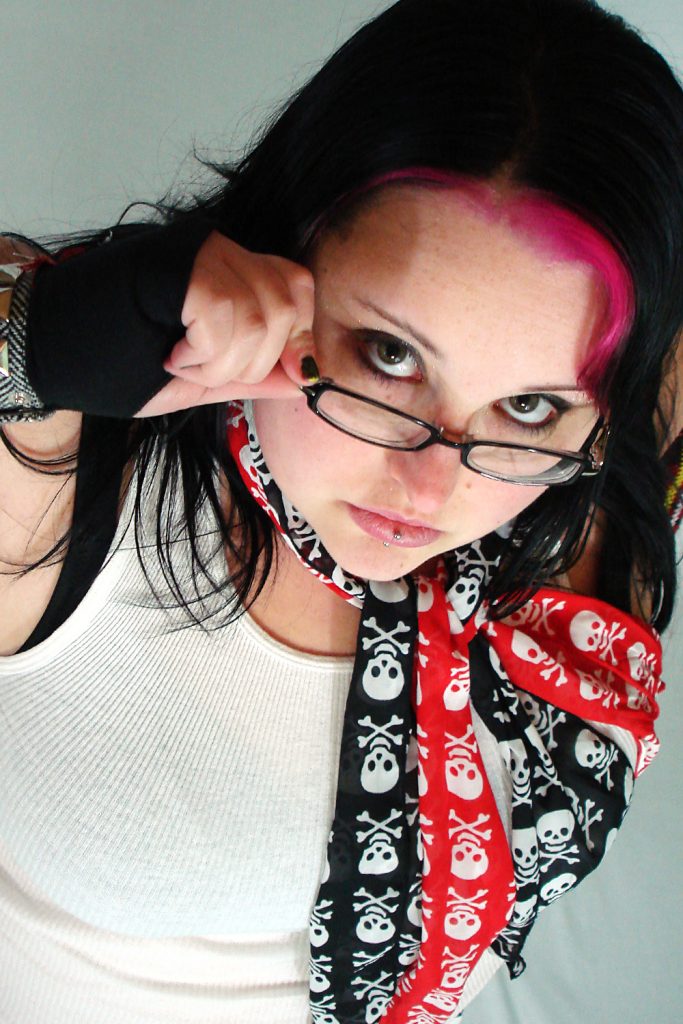 Maranda looks above her glasses at the camera wearing skull print scarves and punk accessories.