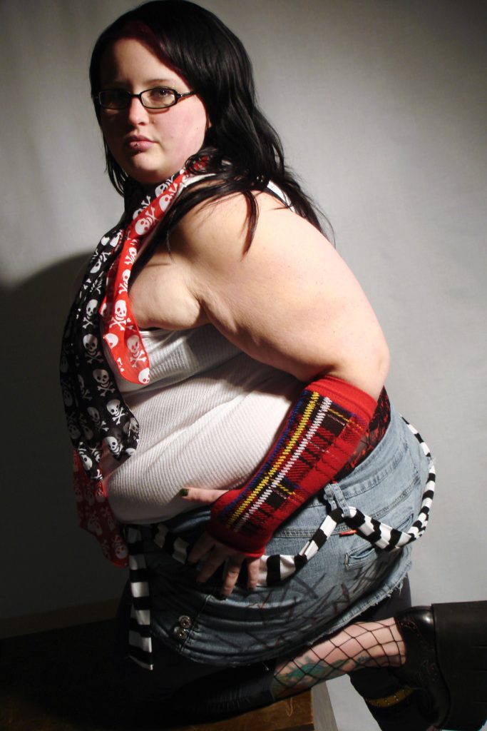 Side profile shot of plus size model with long black hair wearing skull scarves and punk accessories in dramatic lighting.