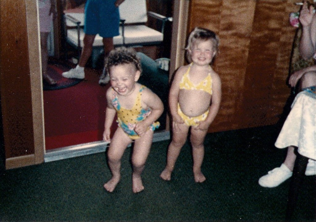 Old Polaroid photo of two young girls in bathing suits laughing.
