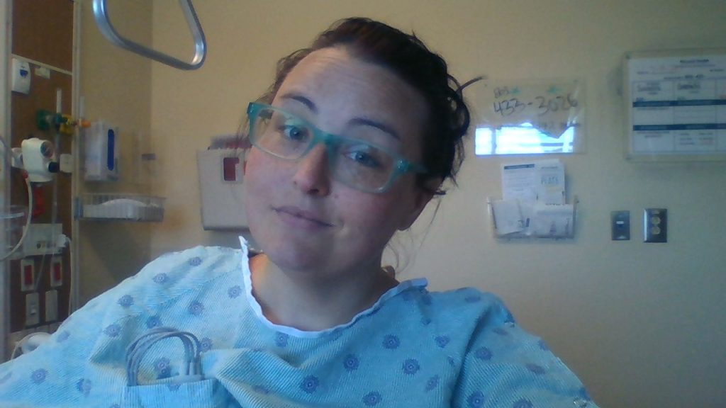 Selfie photo of Maranda in the hospital wearing hospital gown with attached heart monitor.