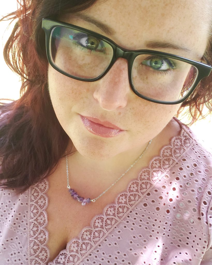 Maranda, a plus size woman wearing nerdy black glasses, models a handmade amethyst gem chip bar necklace from Awaken Gemini.