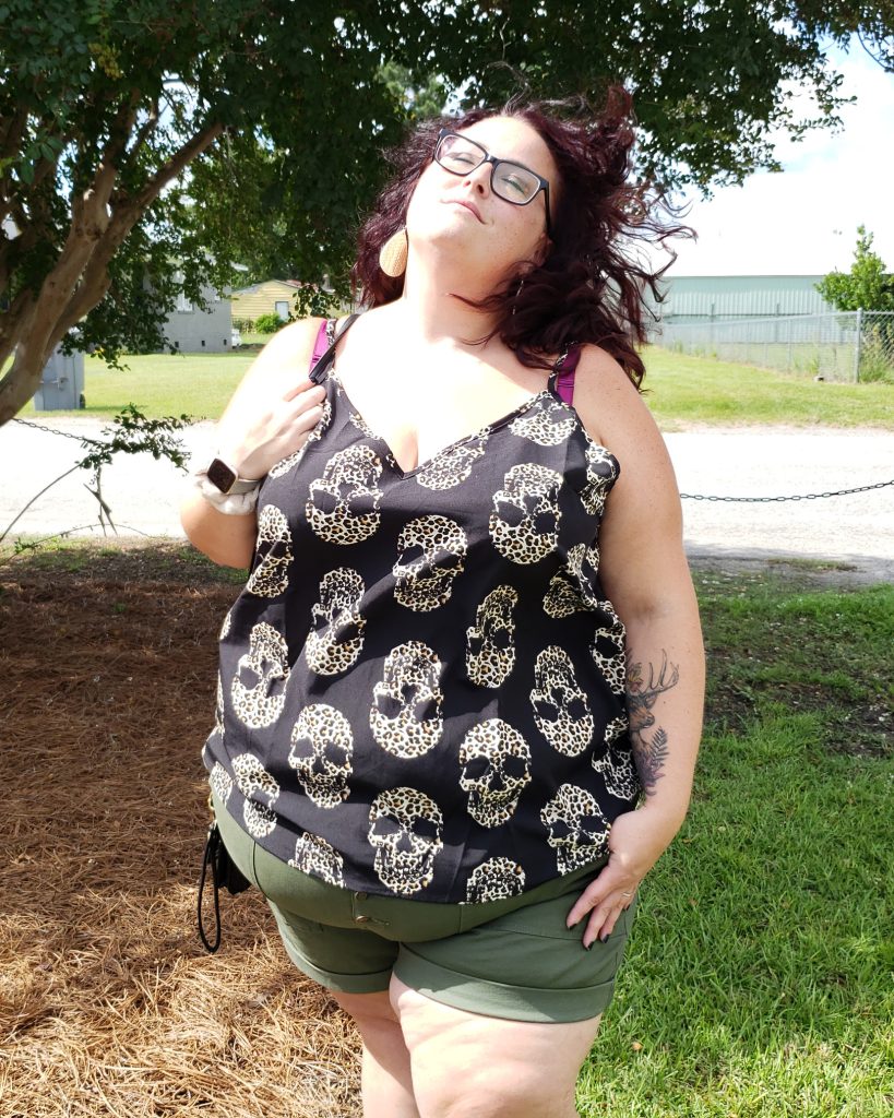 Maranda, a plus size woman wearing a tank top and shorts, stands in full sun with hair blowing in the breeze.