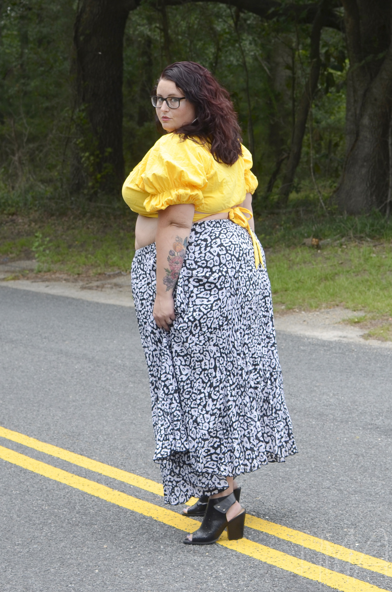 Maranda, a plus size woman, stands in the middle of the roadway wearing a black and white leopard print maxi skirt and yellow tie-back crop top.