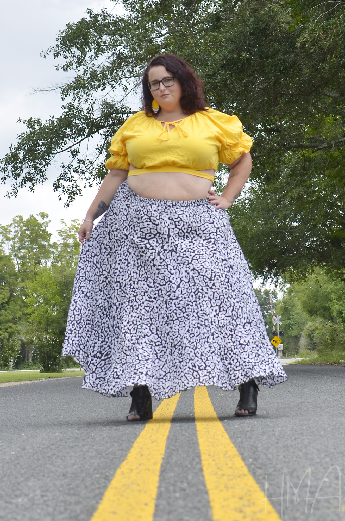 Maranda, a plus size woman, models a leopard print maxi skirt with yellow crop top, standing over the center line of a road.