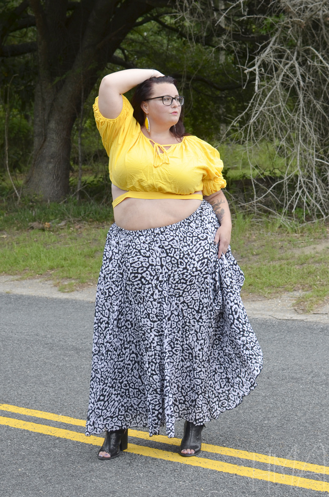 Maranda, a plus size woman, stands in the center of the road modeling a flowy maxi skirt and yellow crop top.