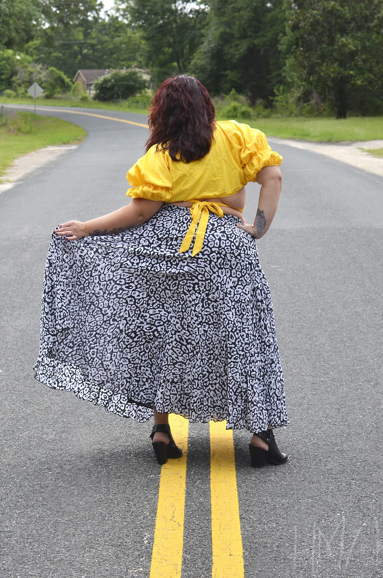 Maranda, a plus size woman, faces away from the camera in the center of the road to show the back of her leopard print maxi skirt and tie-back crop top.