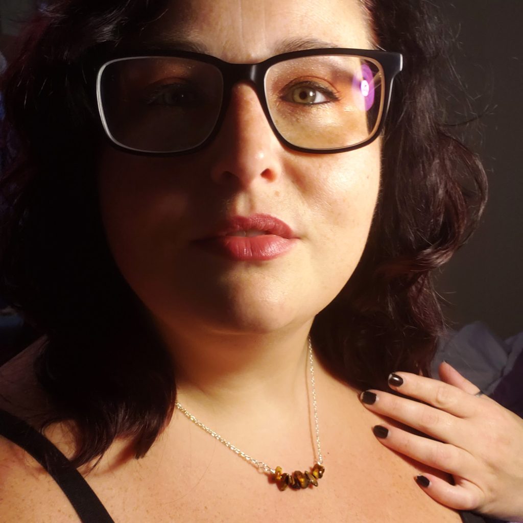 Maranda, a plus size woman with dark hair and glasses, models a handmade gem chip bar necklace featuring tiger's eye beads.