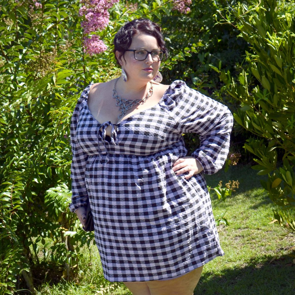 Maranda, a plus size woman, models a black and purple gingham muse dress from Wild Fable outdoors in sunshine.