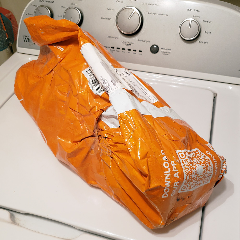 A damaged plastic shipping bag, fully orange in color, displaying Temu's logo, shows tears and scuffs from transit damage.