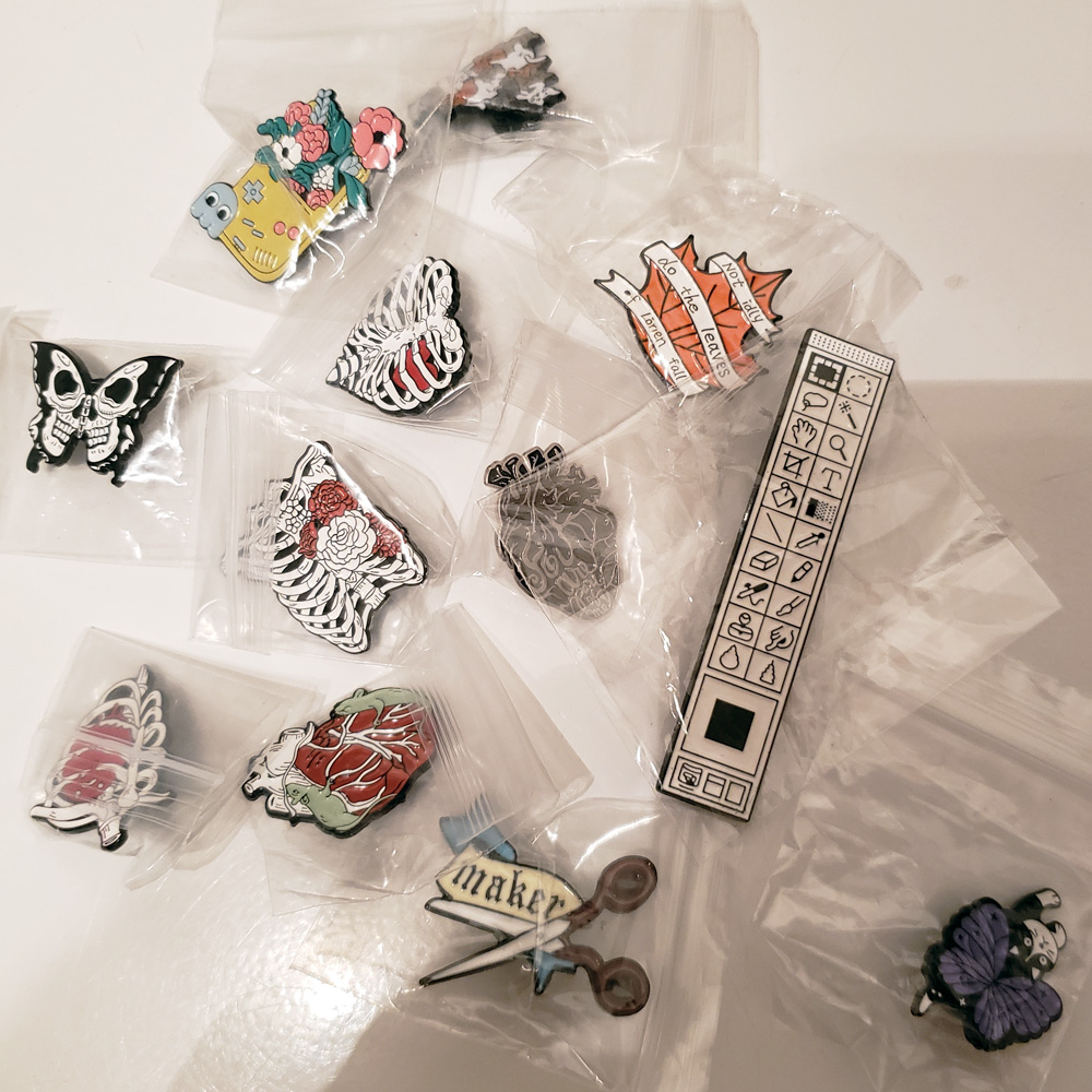 A collection of enamel pins with random designs is displayed, still in plastic packaging as received from Temu.