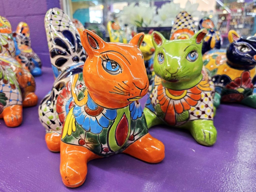 Colorfully hand-painted squirrel or chipmunk ceramic garden figures posed on a purple shelf at South of the Border's Mexico Shop East.