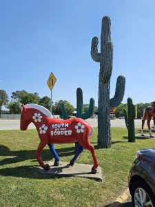 Red horse statue painted with South of the Border logo and large cacti sculptures along the side of the road.